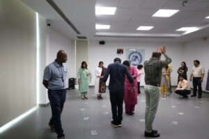 Group of people standing in a conference room, each person facing different directions, with numbered cards on the floor for an activity or exercise.